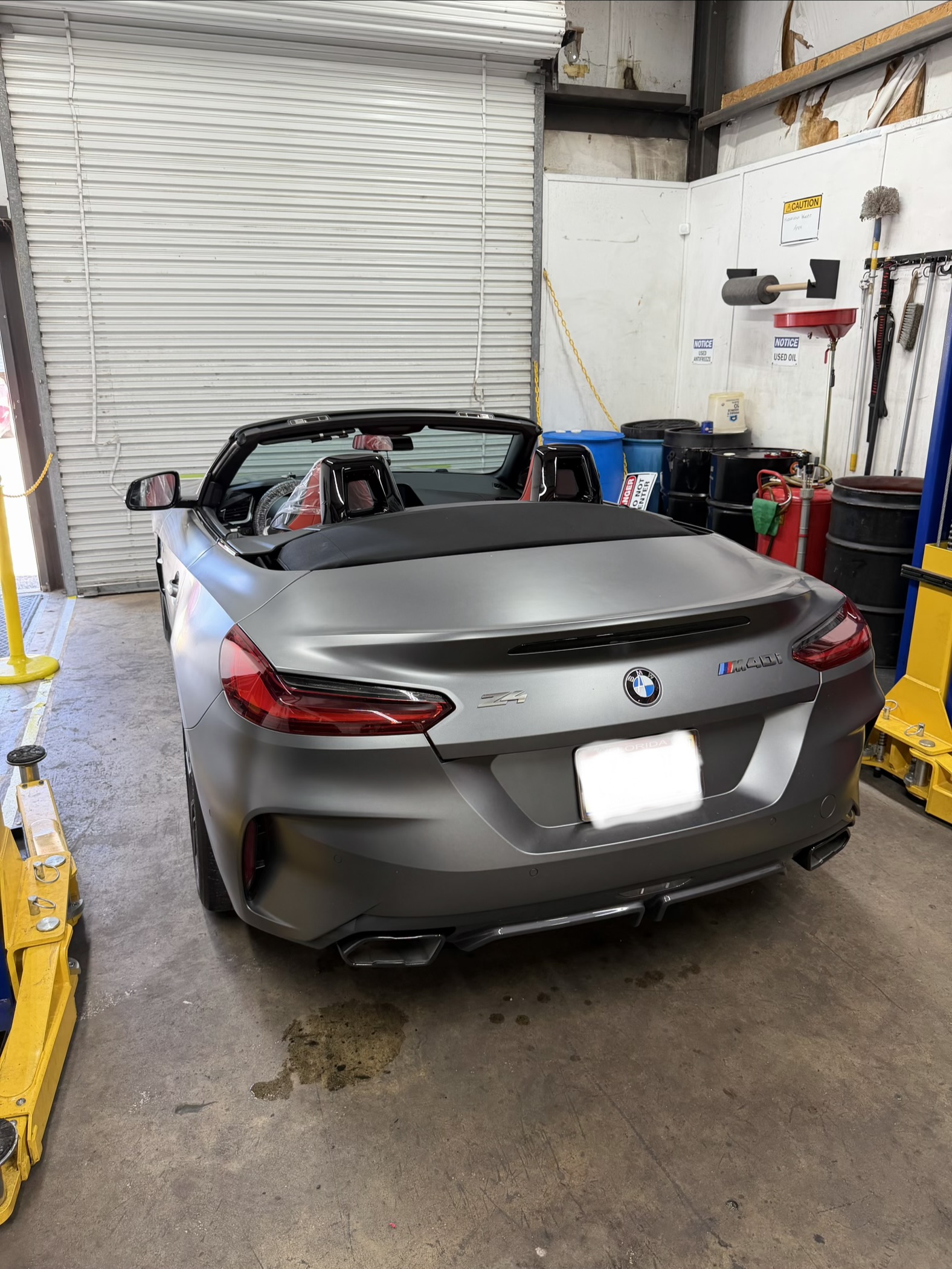 Rear view of a grey BMW Z4 convertible inside the garage, with its license plate obscured